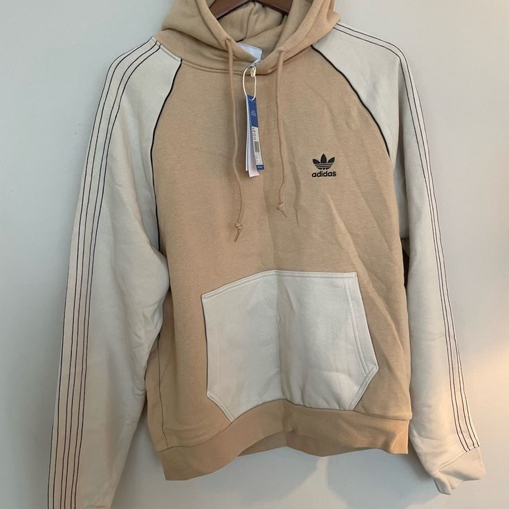 Beige and white Adidas hoodie with a tag on a light gray background