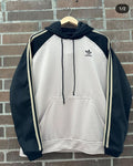Black and white Adidas hoodie on a hanger against a brick wall.