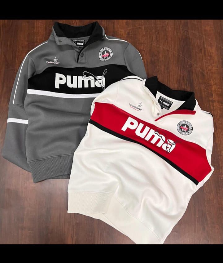 Gray and white Puma sweatshirt and red and white Puma polo shirt on a wooden surface