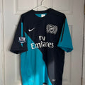 Black and blue sports jersey with Emirates logo on a hanger against a white door.