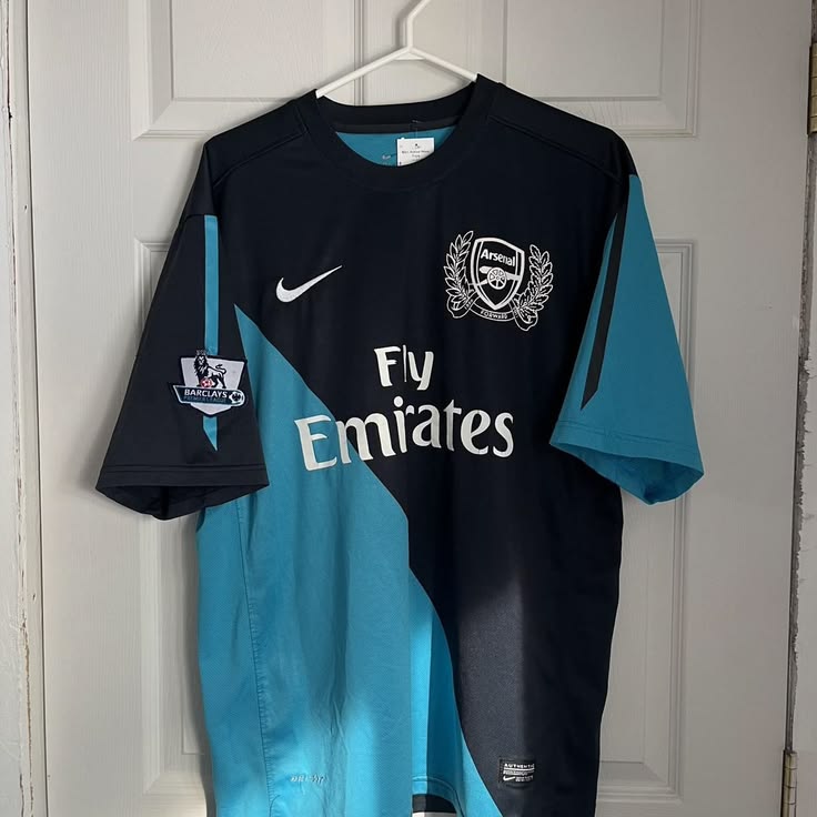 Black and blue sports jersey with Emirates logo on a hanger against a white door.