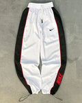 White and black Nike tracksuit pants with red accents on a gray surface